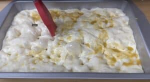 Spreading olive oil over focaccia dough with a red brush in a baking pan.